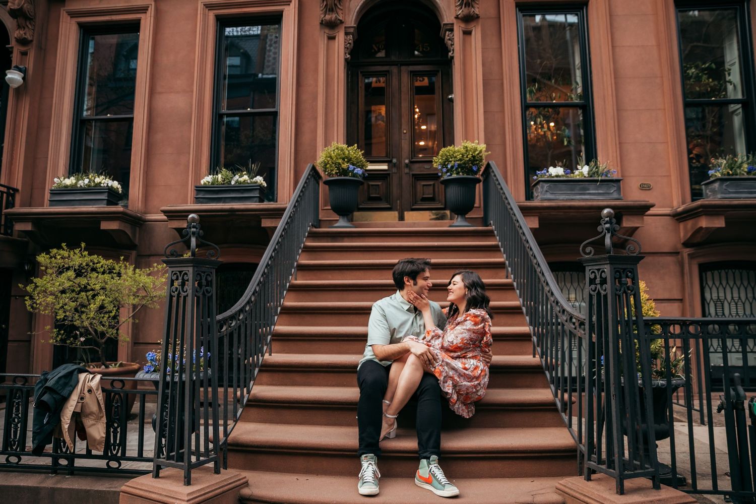 Romantic couple sharing intimate moment seated on classic NYC brownstone staircase outdoors.