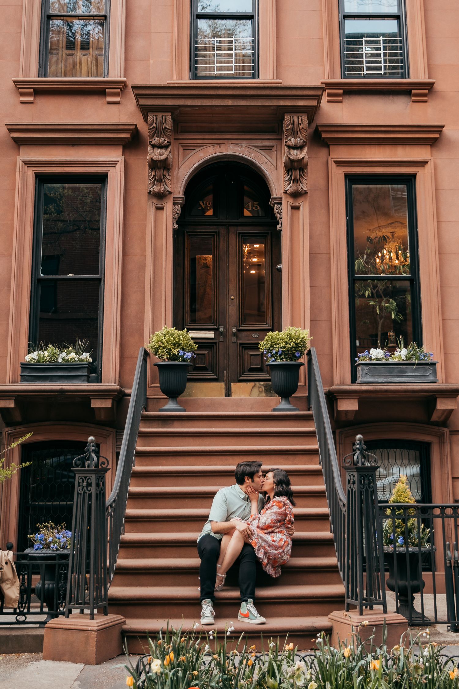 Couple sharing a kiss on the steps of a beautiful historic brownstone building in New York.