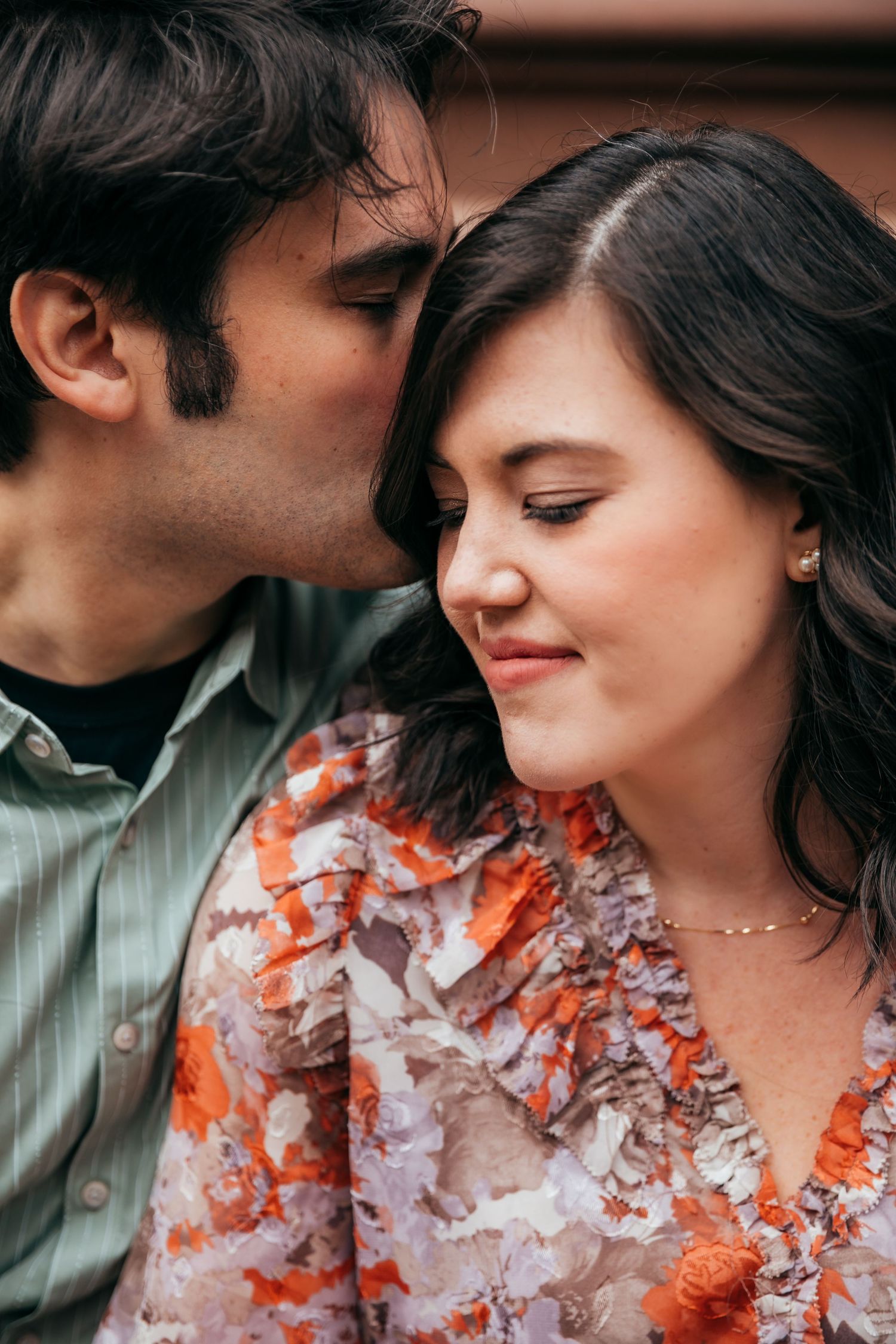 Man gently kissing woman on cheek as she smiles softly during romantic couples portrait session.