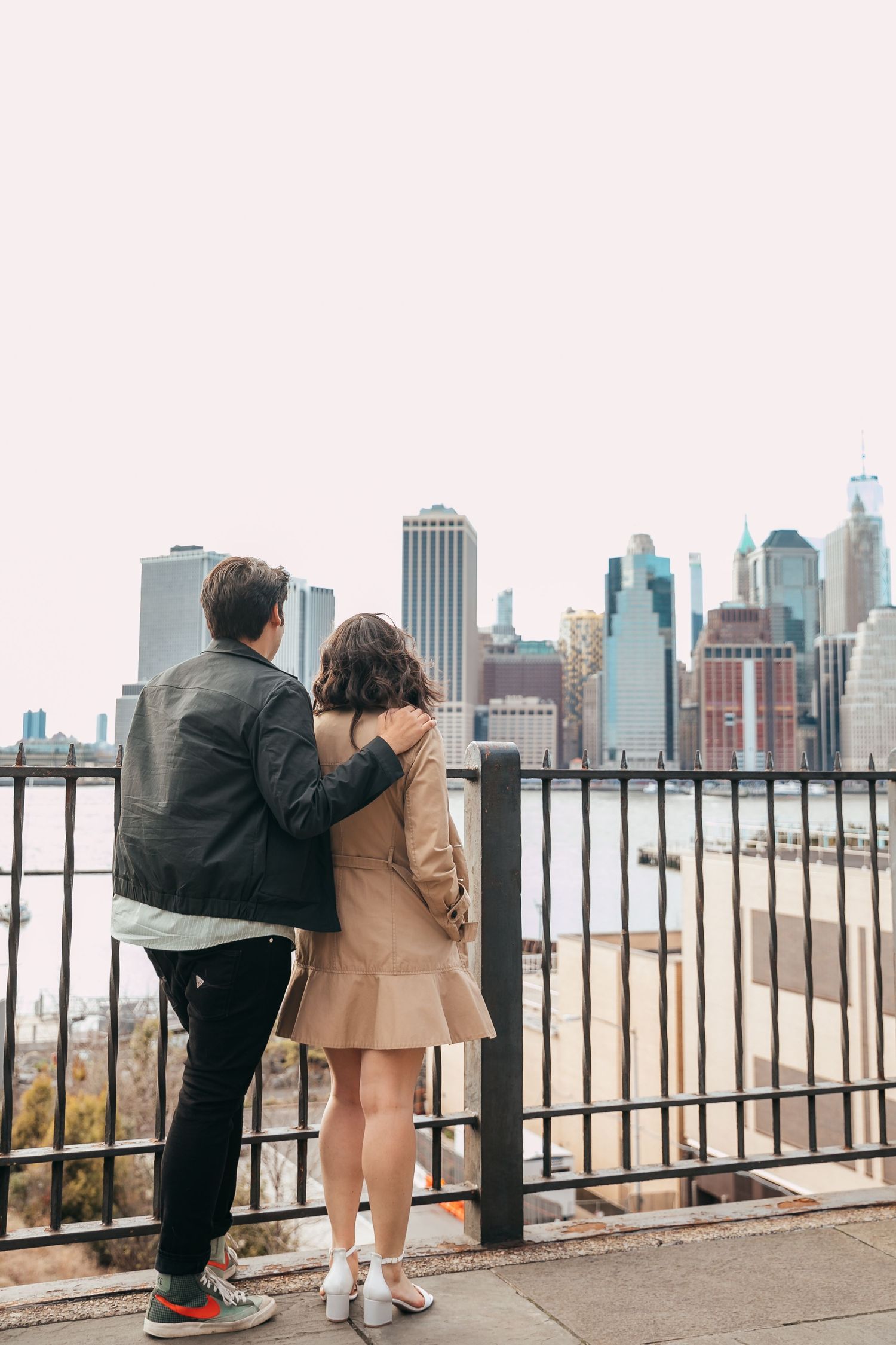 Couple embracing while overlooking stunning Manhattan skyline from Brooklyn waterfront promenade.