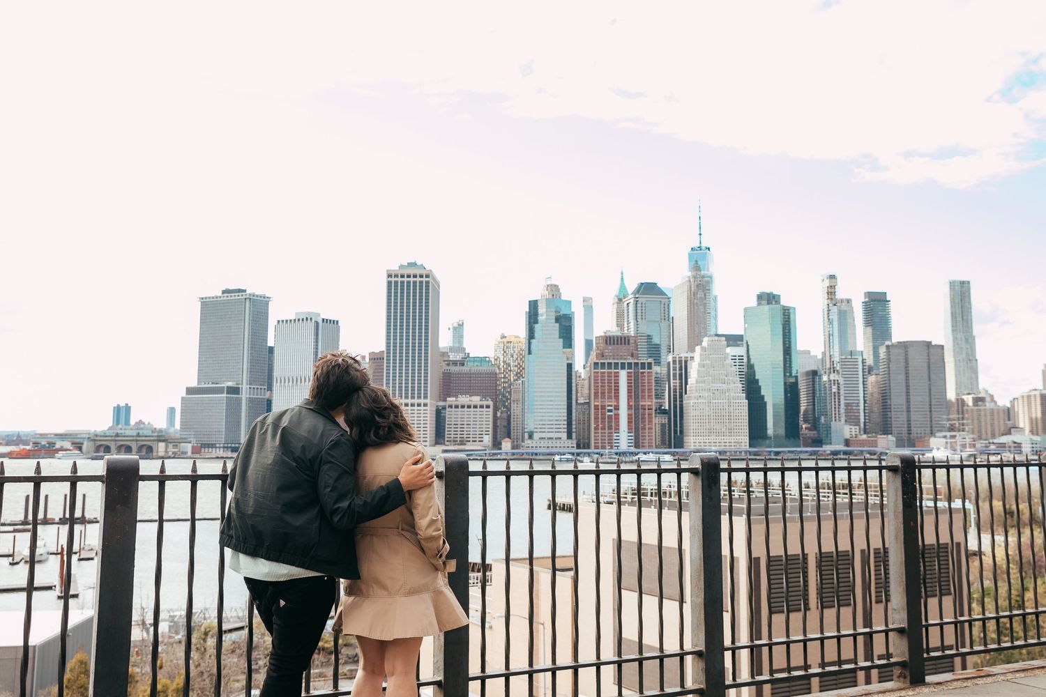Couple embracing while overlooking the Manhattan skyline from Brooklyn waterfront.