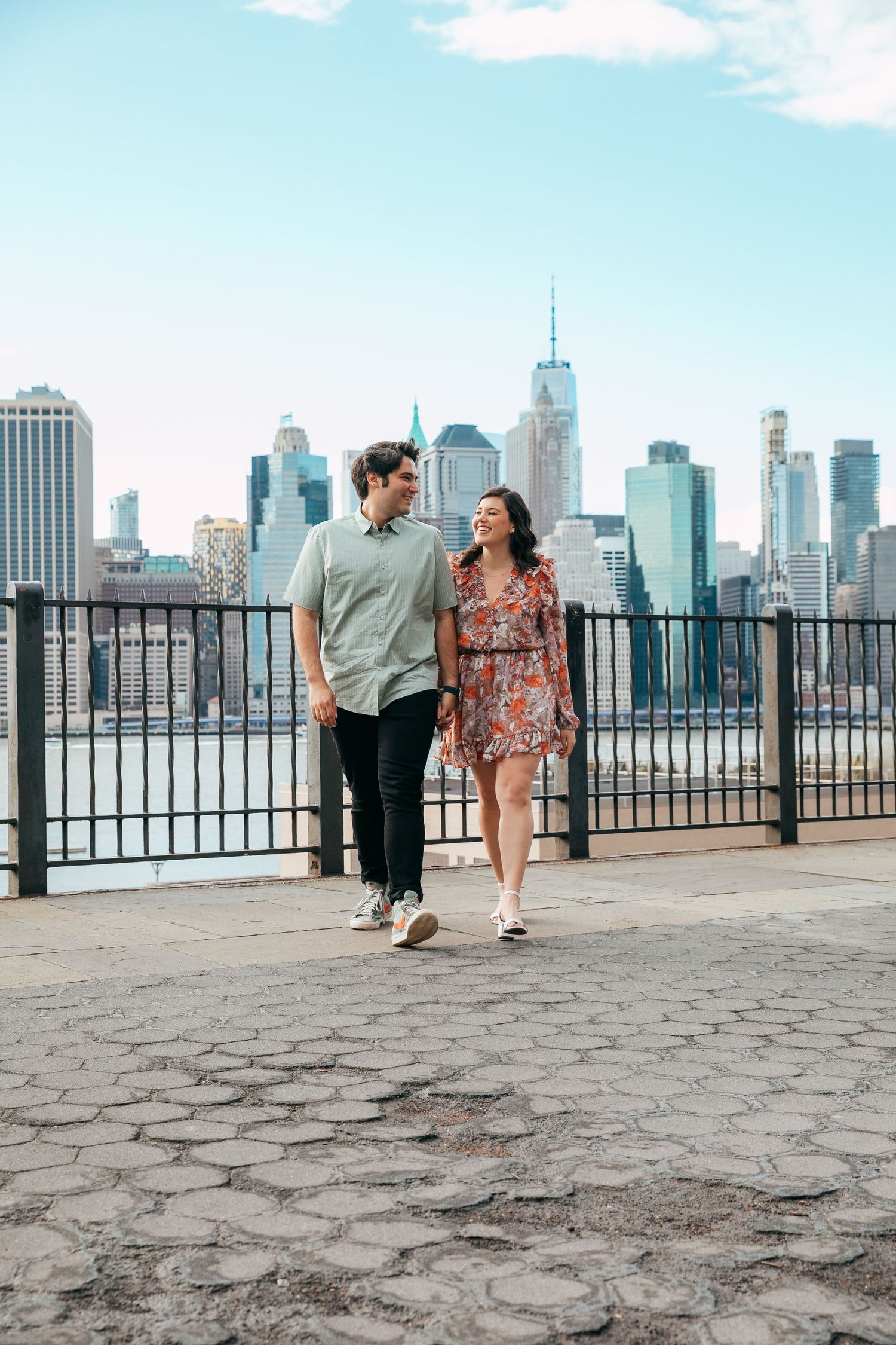 Happy couple walking hand in hand with NYC skyline backdrop on sunny day.