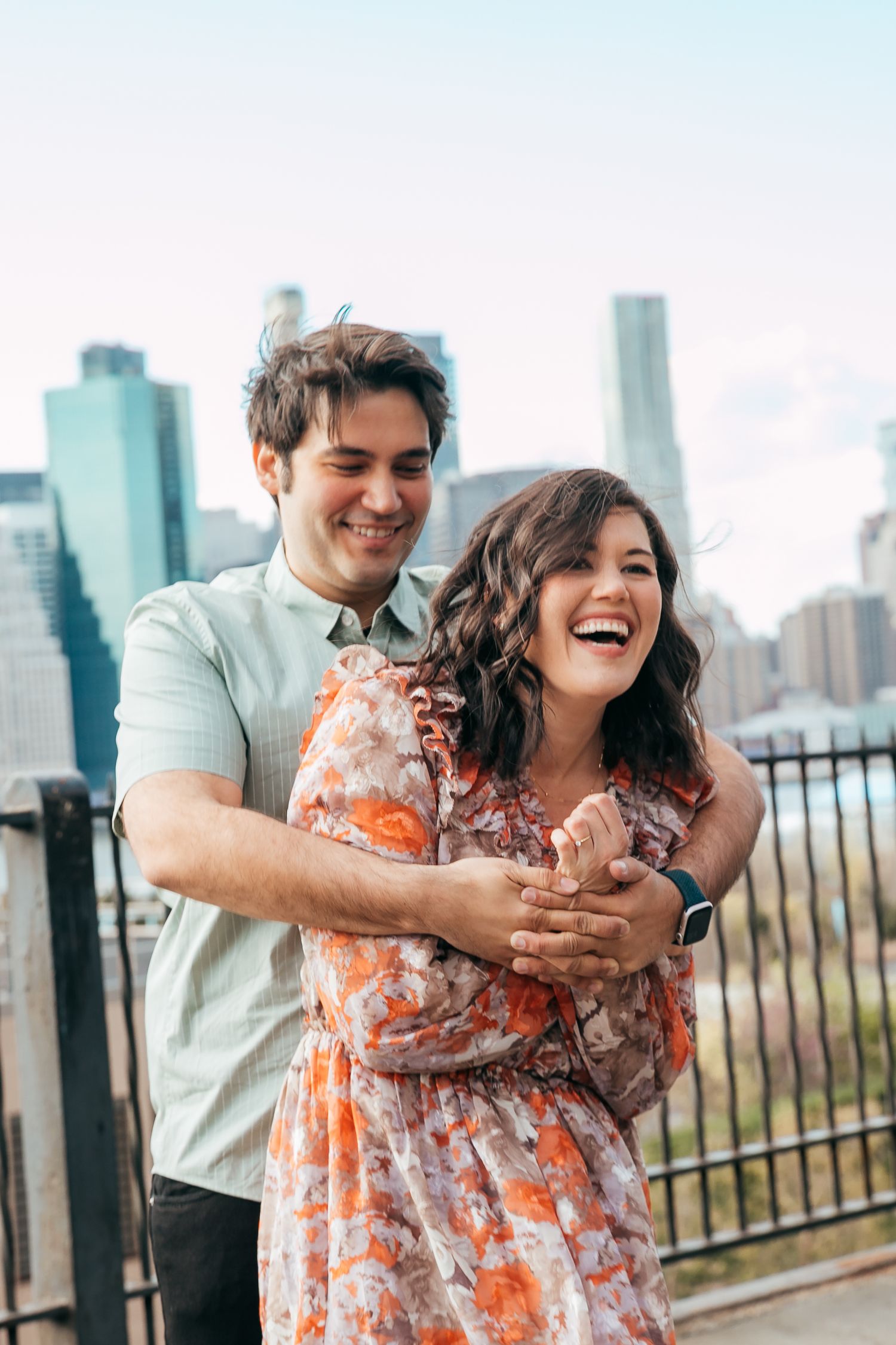 Couple laughing and hugging closely with New York City skyline in the background.