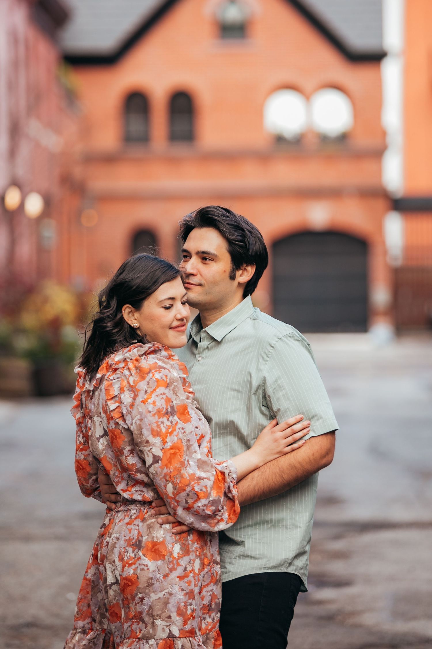 Loving couple embracing warmly on a cobblestone street with a blurred red brick building backdrop.