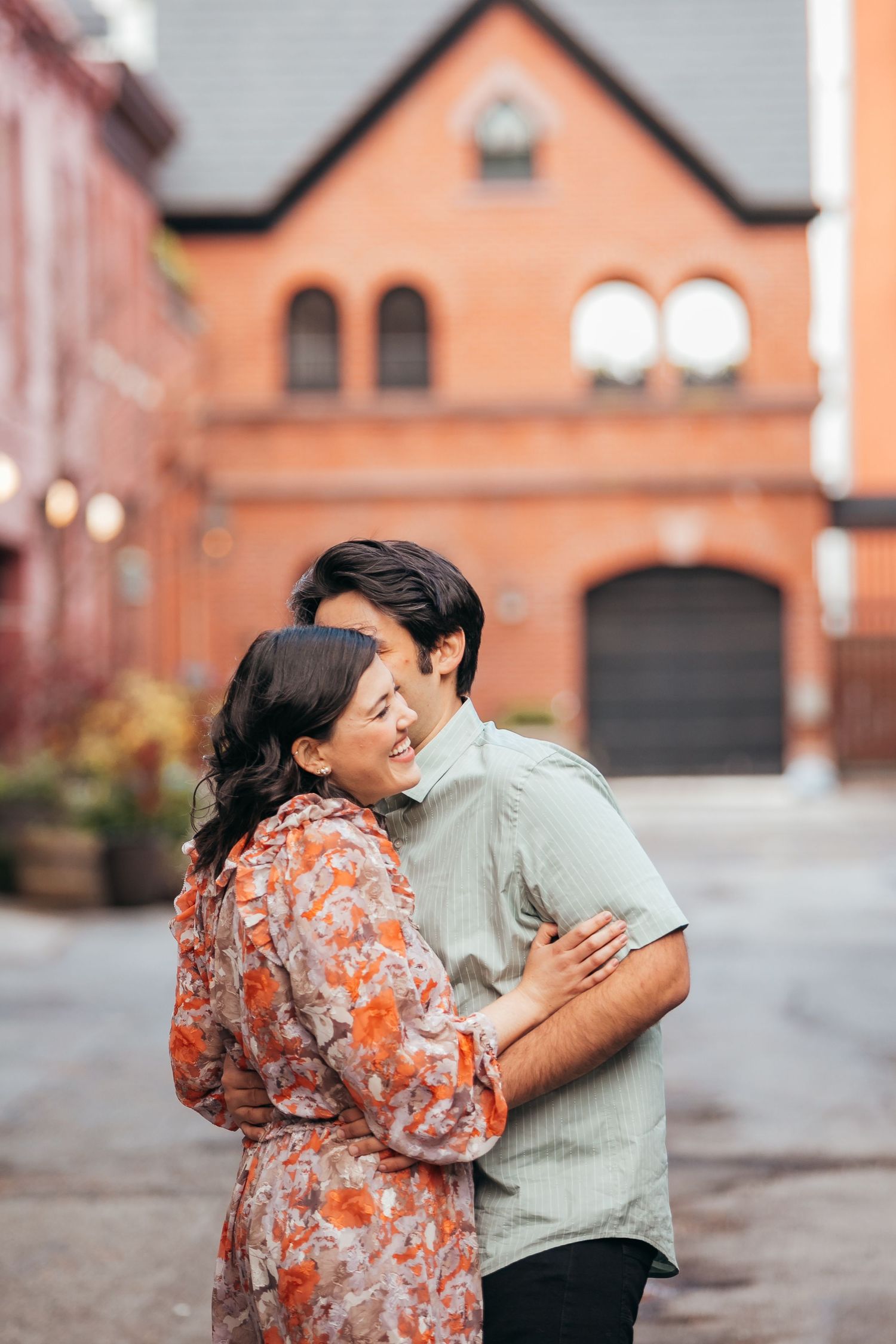 Joyful couple sharing a warm embrace while smiling at each other near a charming red brick building.