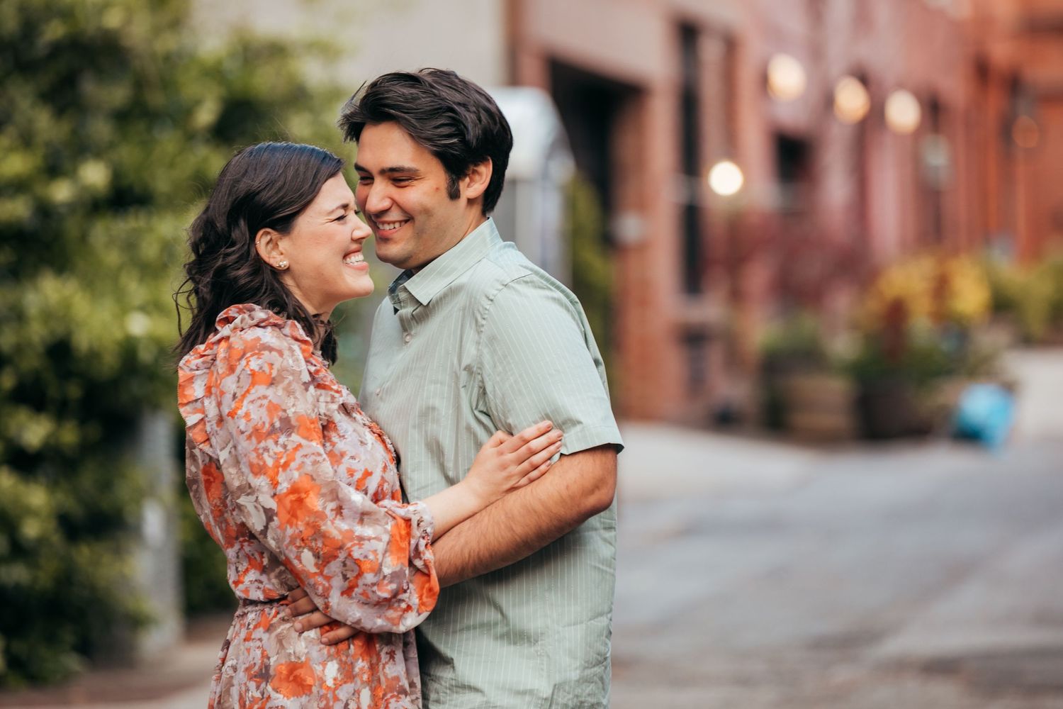 Smiling couple embracing affectionately on a charming brick-lined street with soft natural lighting.