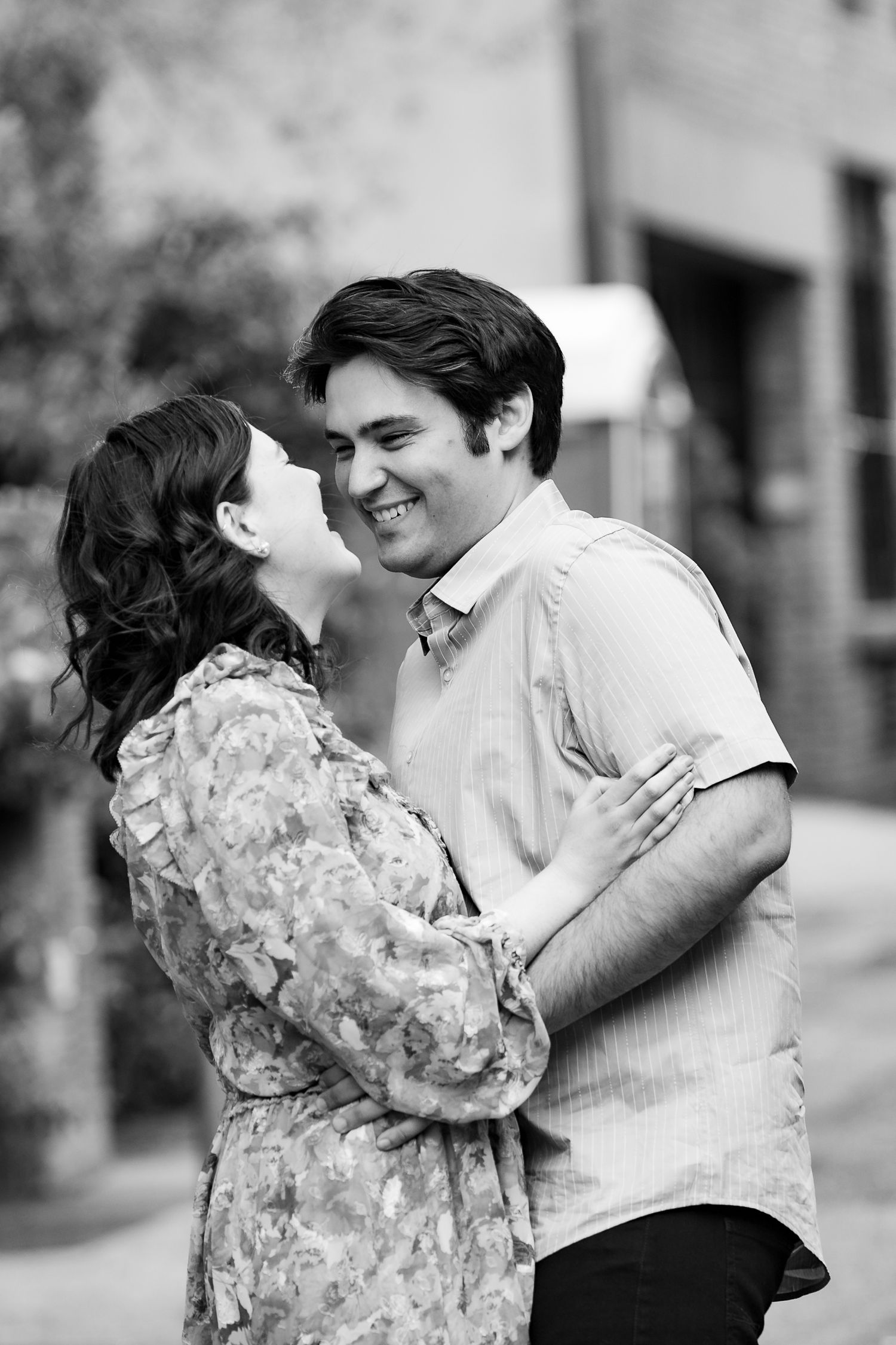 Black and white photo of a laughing couple sharing an intimate moment on a charming urban street.