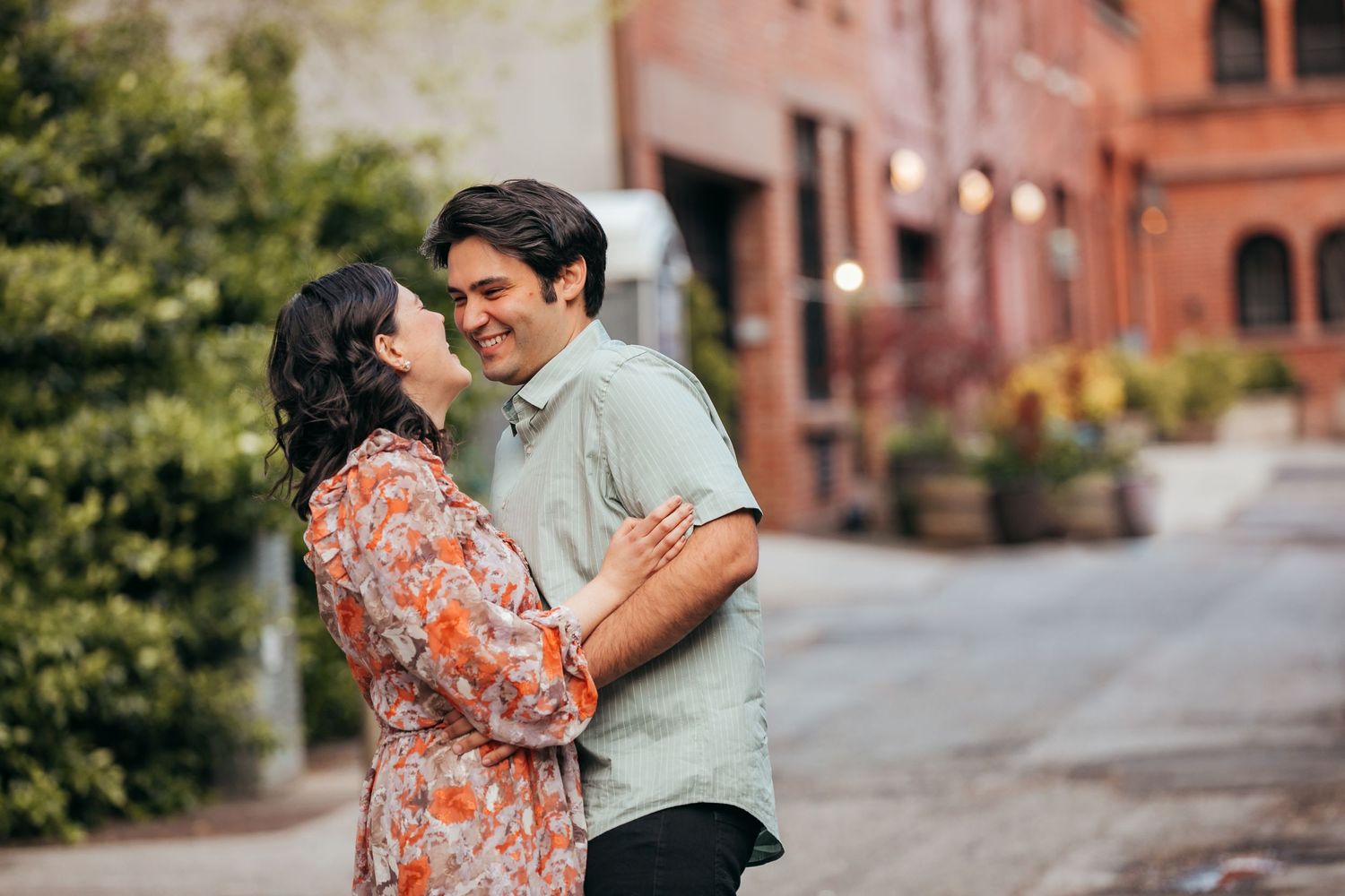 Happy couple sharing a joyful embrace on a sunlit cobblestone street surrounded by lush greenery.