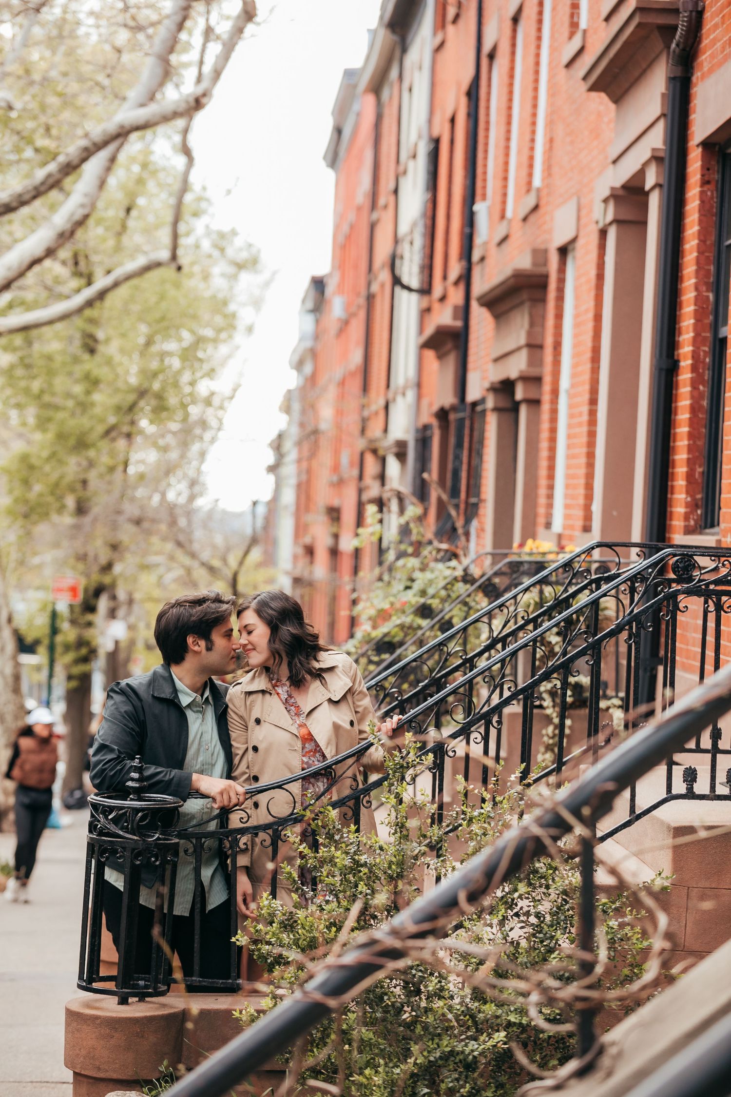 Romantic couple sharing a kiss on brownstone steps along a charming city street.