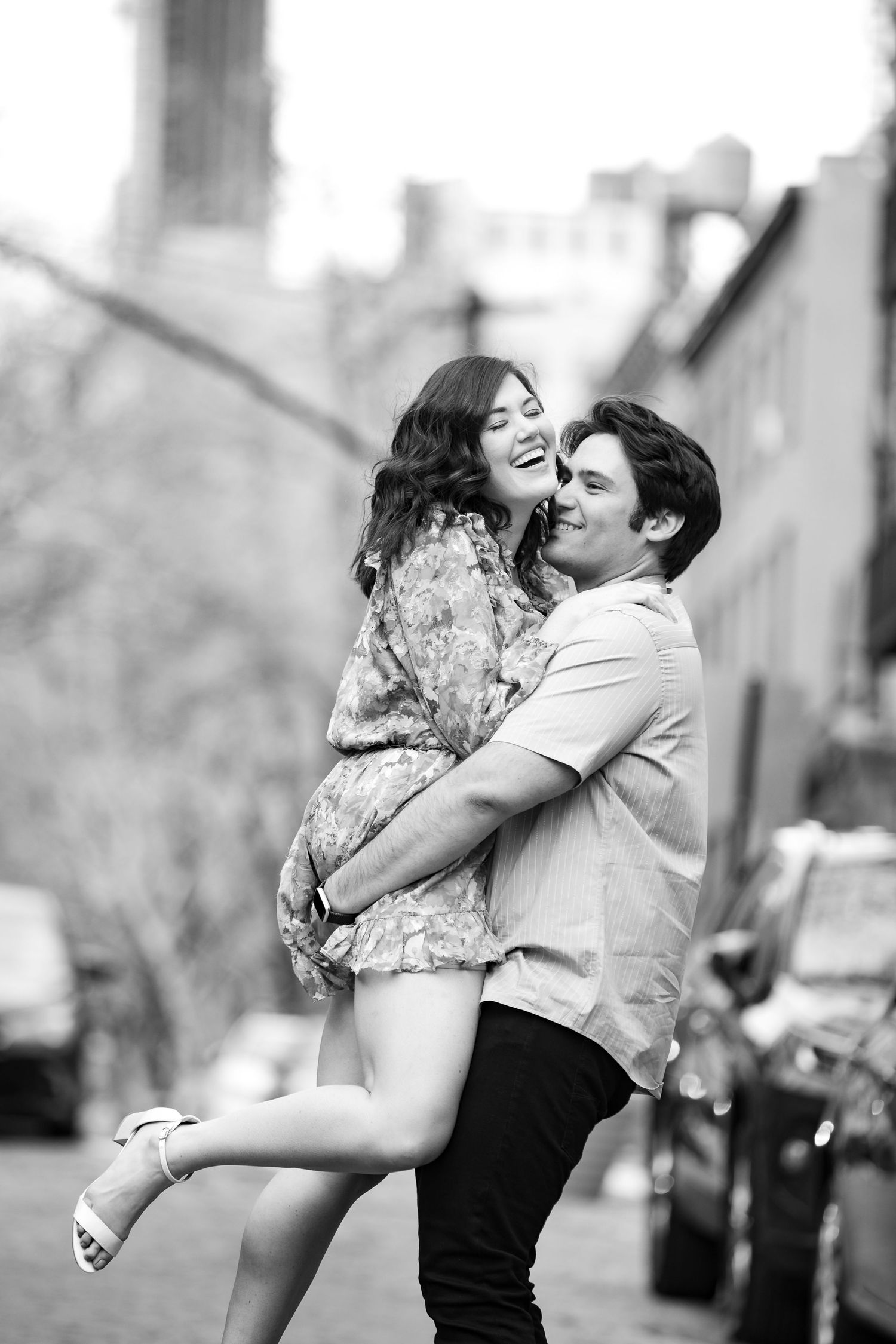 Black and white photo of couple embracing joyfully on a cobblestone city street.