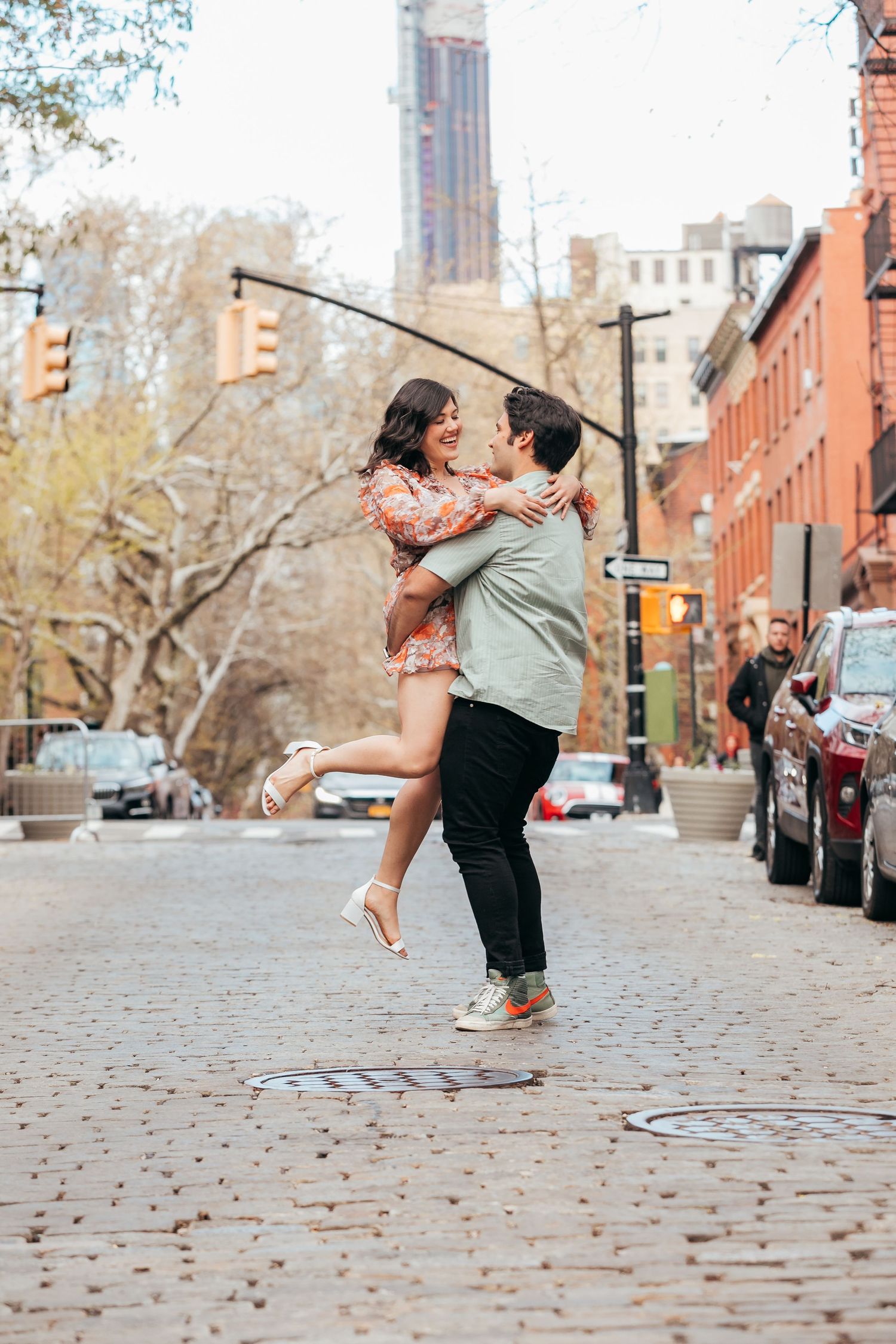 Couple sharing a kiss as man lifts woman on a charming cobblestone city street.