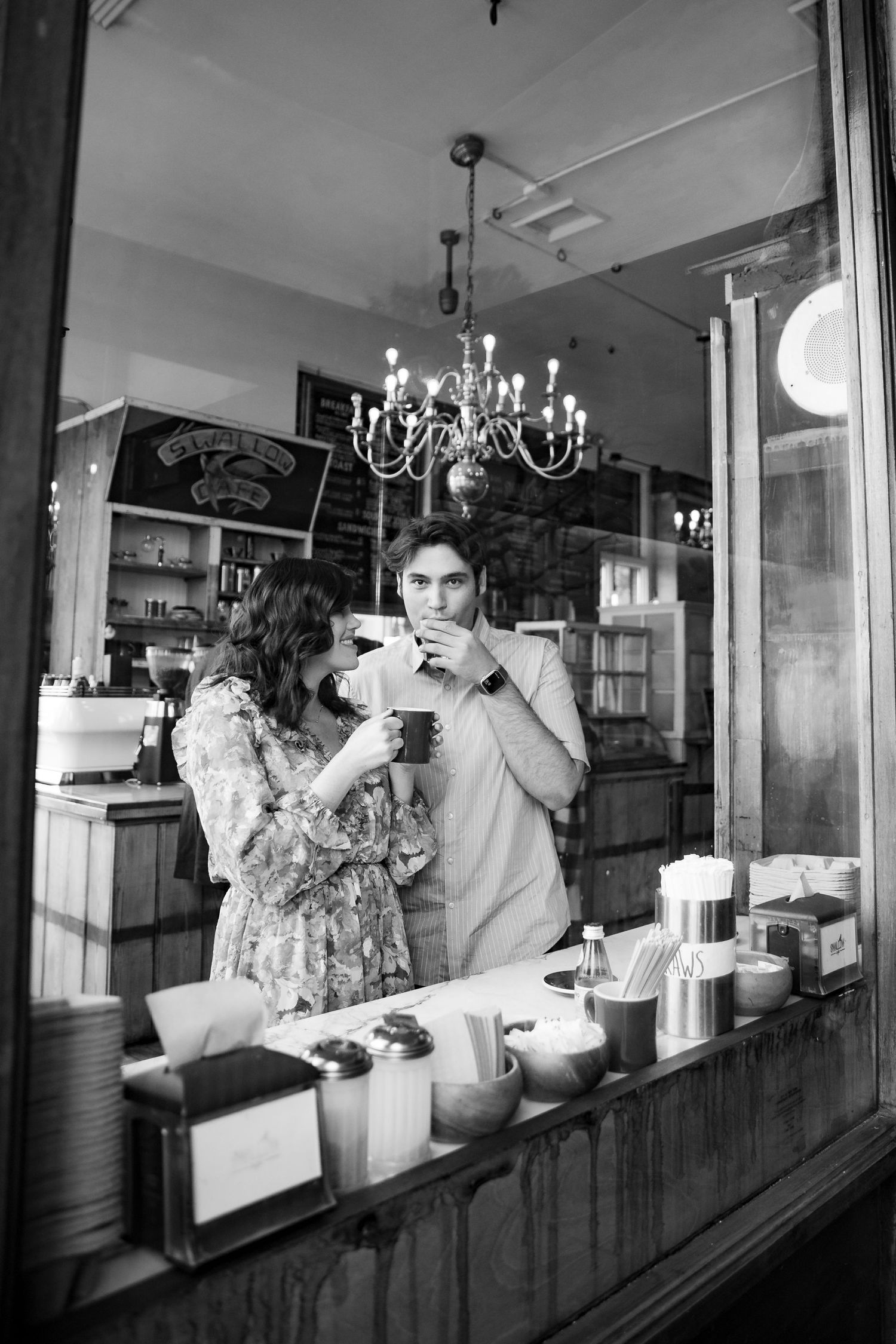 Black and white reflection of couple sharing coffee in a cozy vintage cafe window.