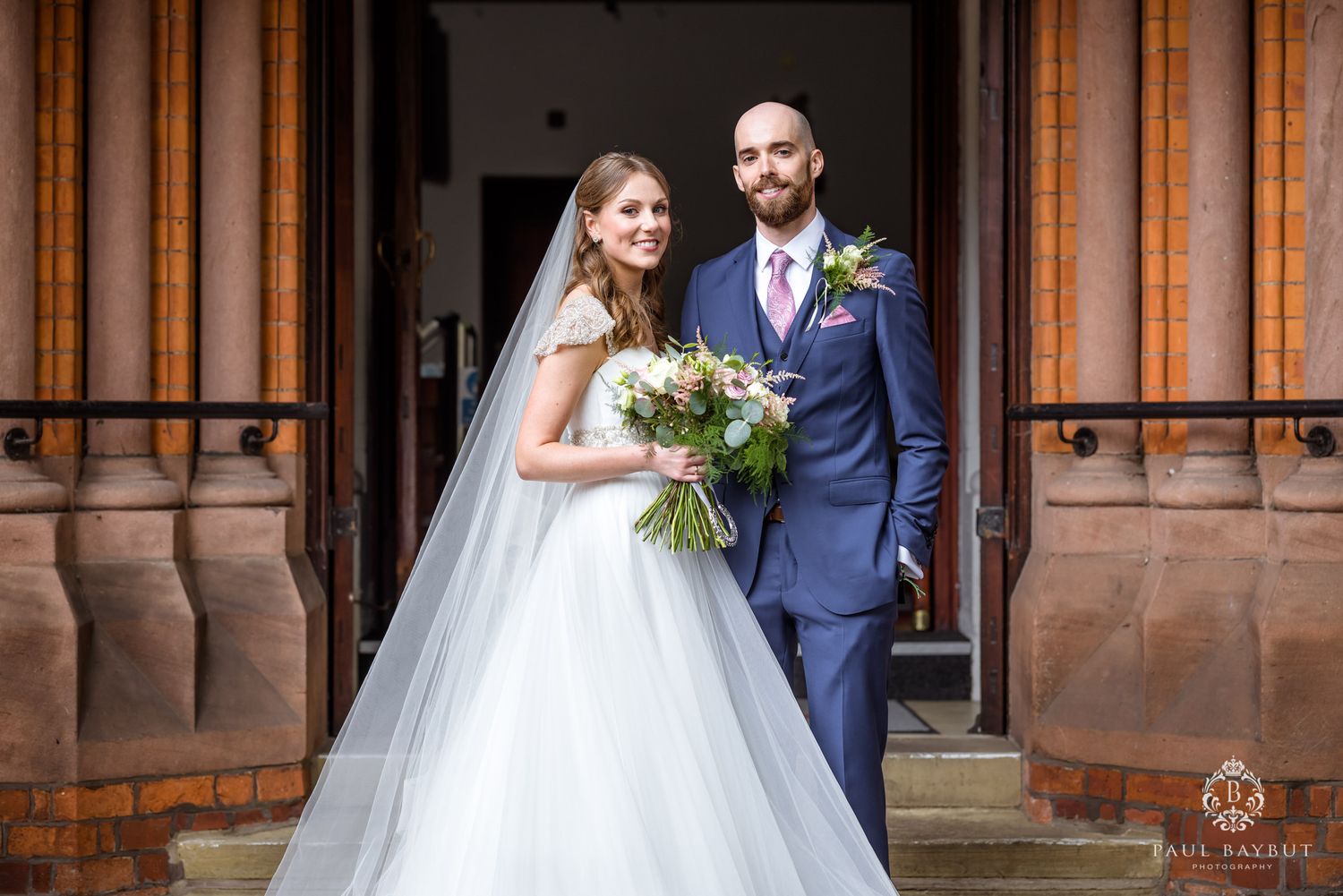Wedding couple pose in front of a historic stone building entrance.