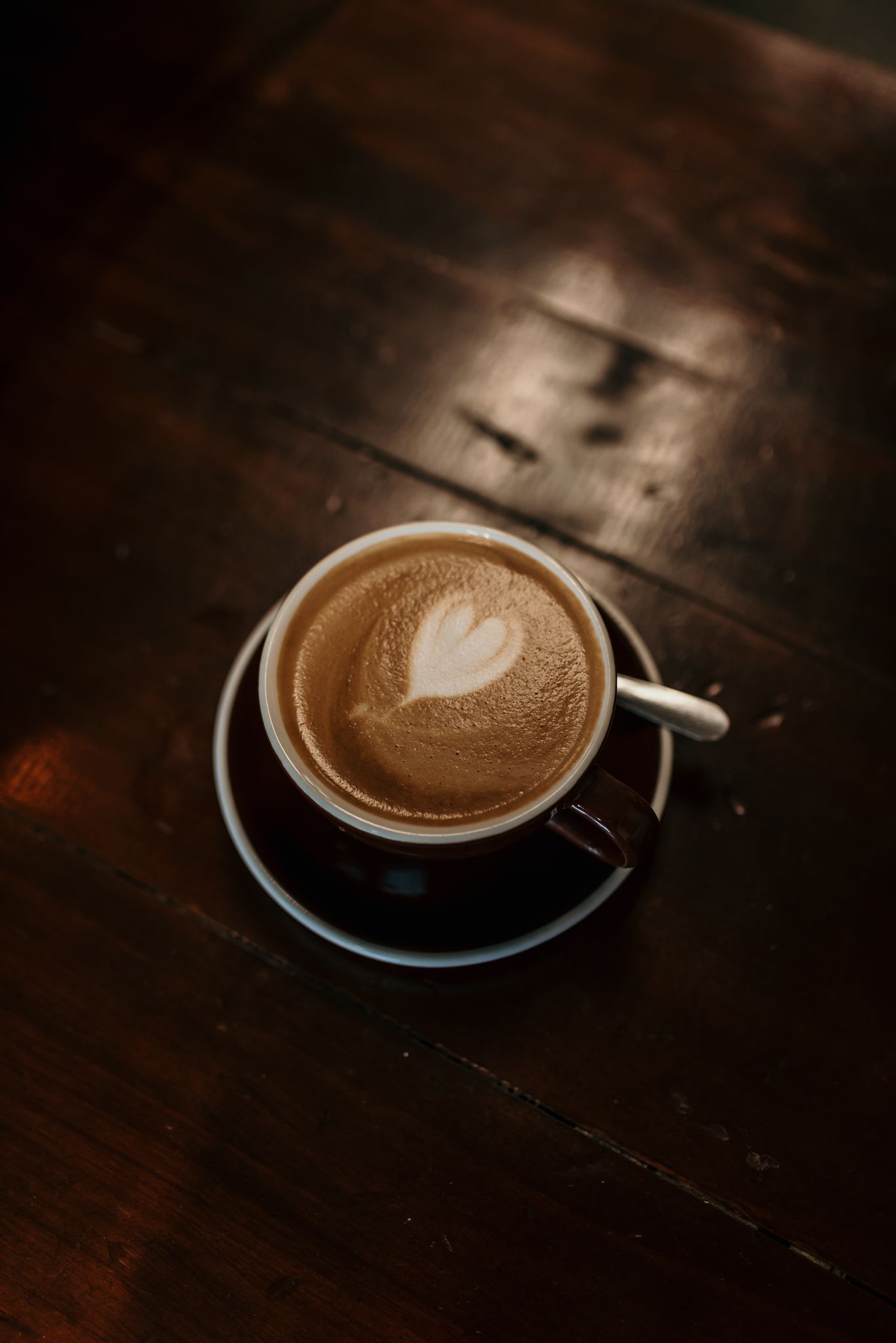 Artisanal latte in white cup with heart-shaped foam art on dark wooden table.