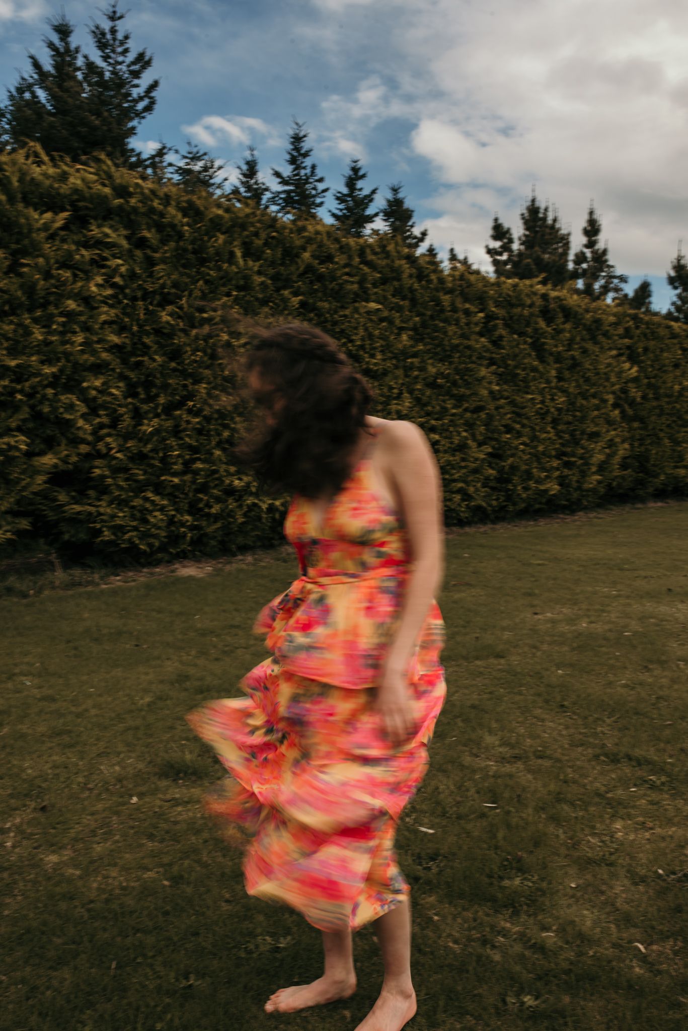 Motion blur of floral dress twirling in garden with evergreen hedge background.