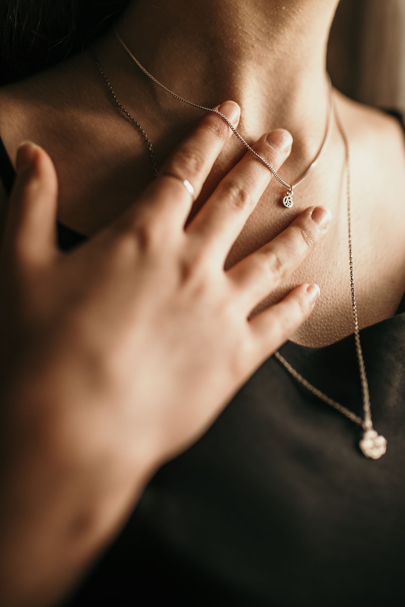 Close-up of delicate layered necklaces and a hand touching collar bone.