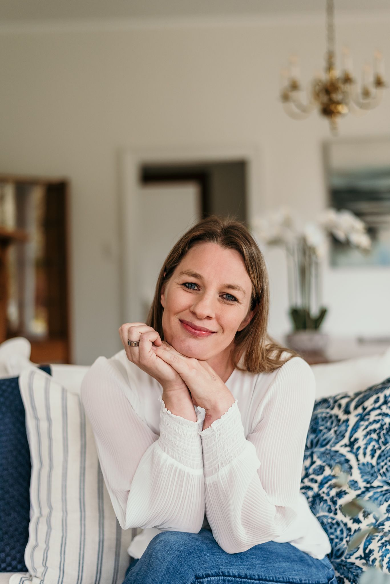 Casual portrait in white sweater on couch with blue and white pillows.