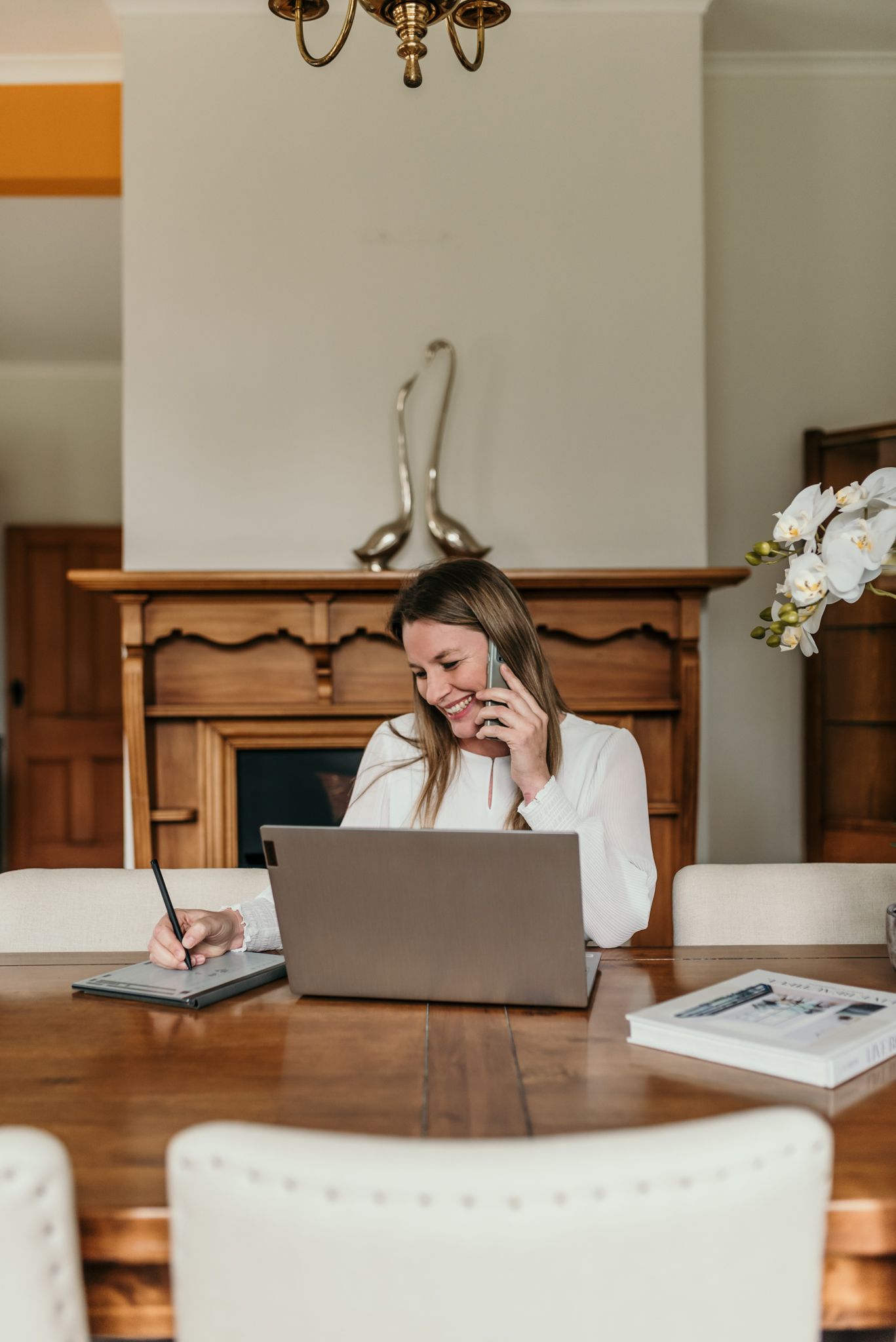 Business professional working on laptop and taking notes while on phone call.