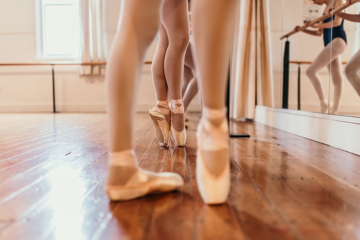 Close-up of ballet pointe shoes and dancers' feet on a polished wooden dance floor.