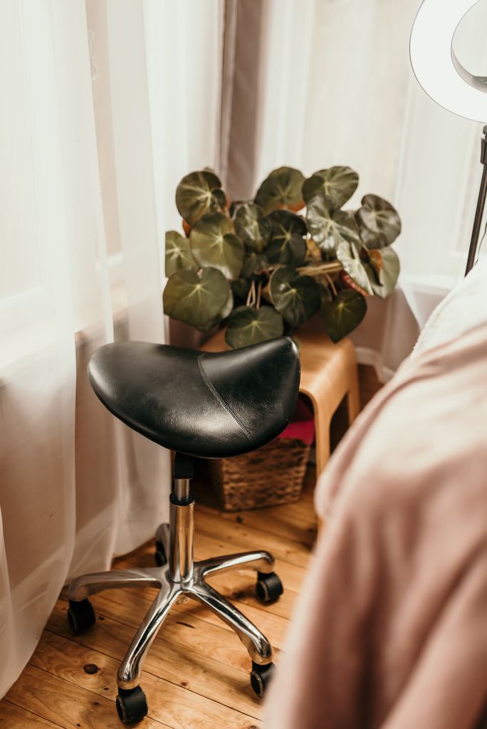 Black rolling stool near potted plants and sheer curtains in a beauty salon setting.