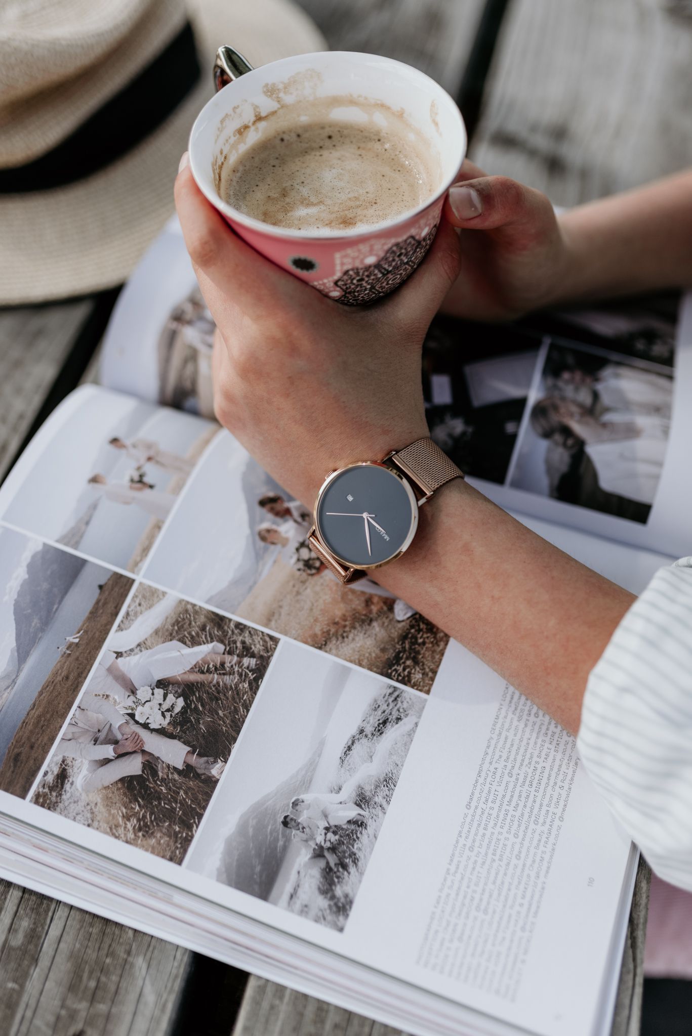 Person reading a book with coffee and wearing a rose gold watch.