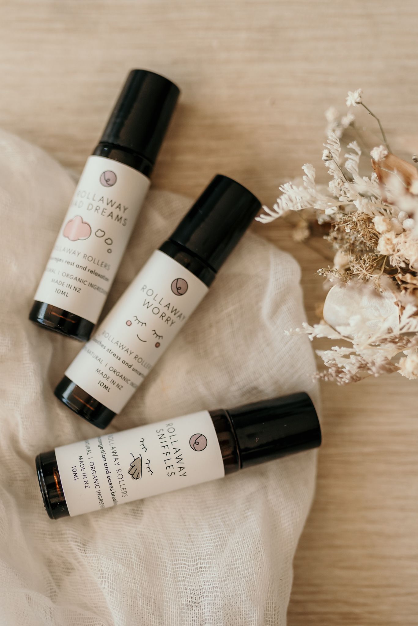 Three natural skincare product bottles arranged with dried flowers on white fabric.