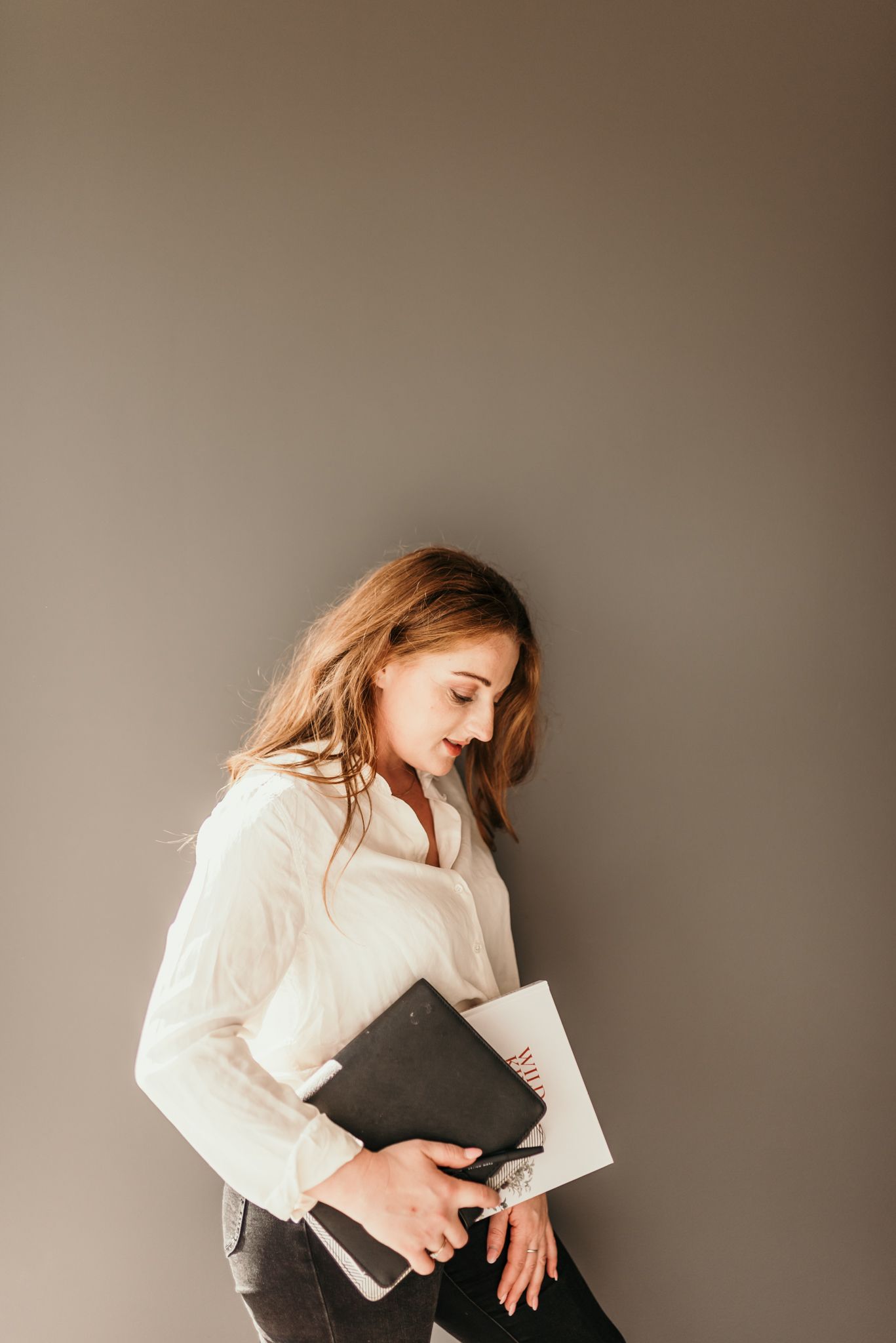 Figure in white shirt holding documents against neutral grey wall.