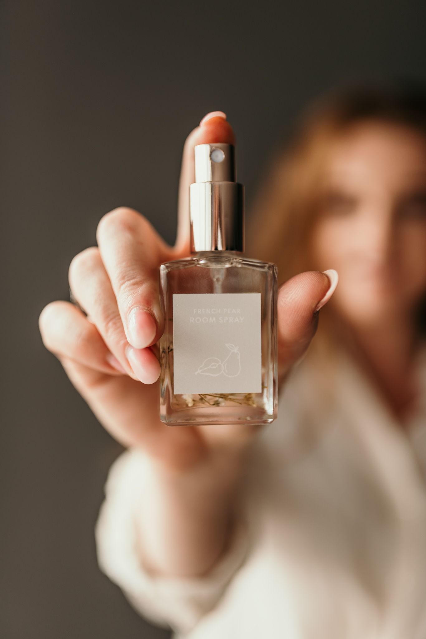 Hand holding up a clear glass perfume bottle against dark background.
