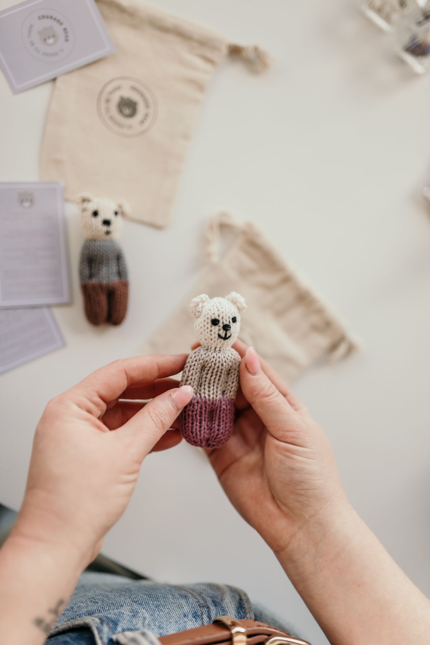 Hands holding a small knitted stuffed animal toy with craft supplies in the background.
