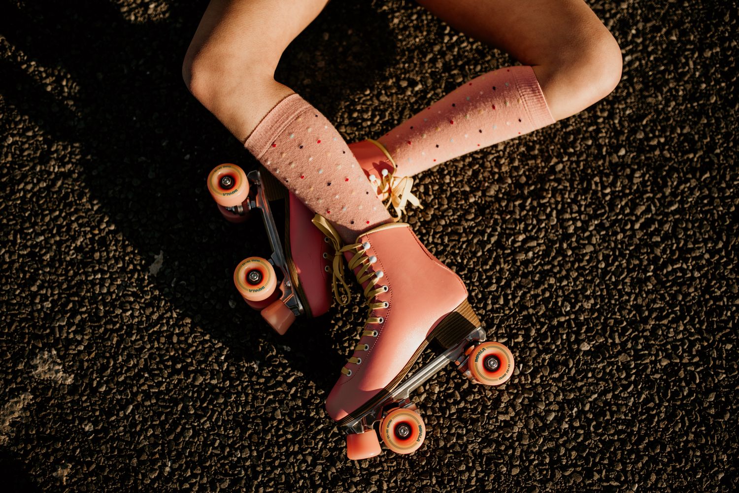 Close-up of pink vintage roller skates with white socks on asphalt.