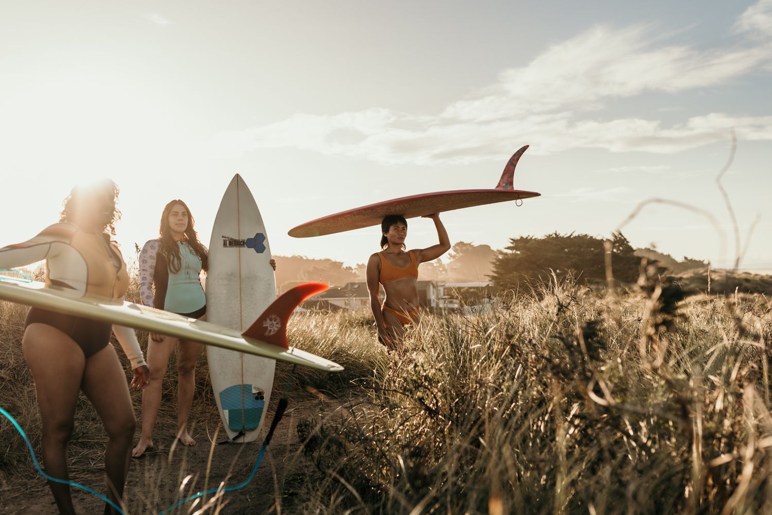 Group of surfers walking along the beach trail with surfboards at sunset.