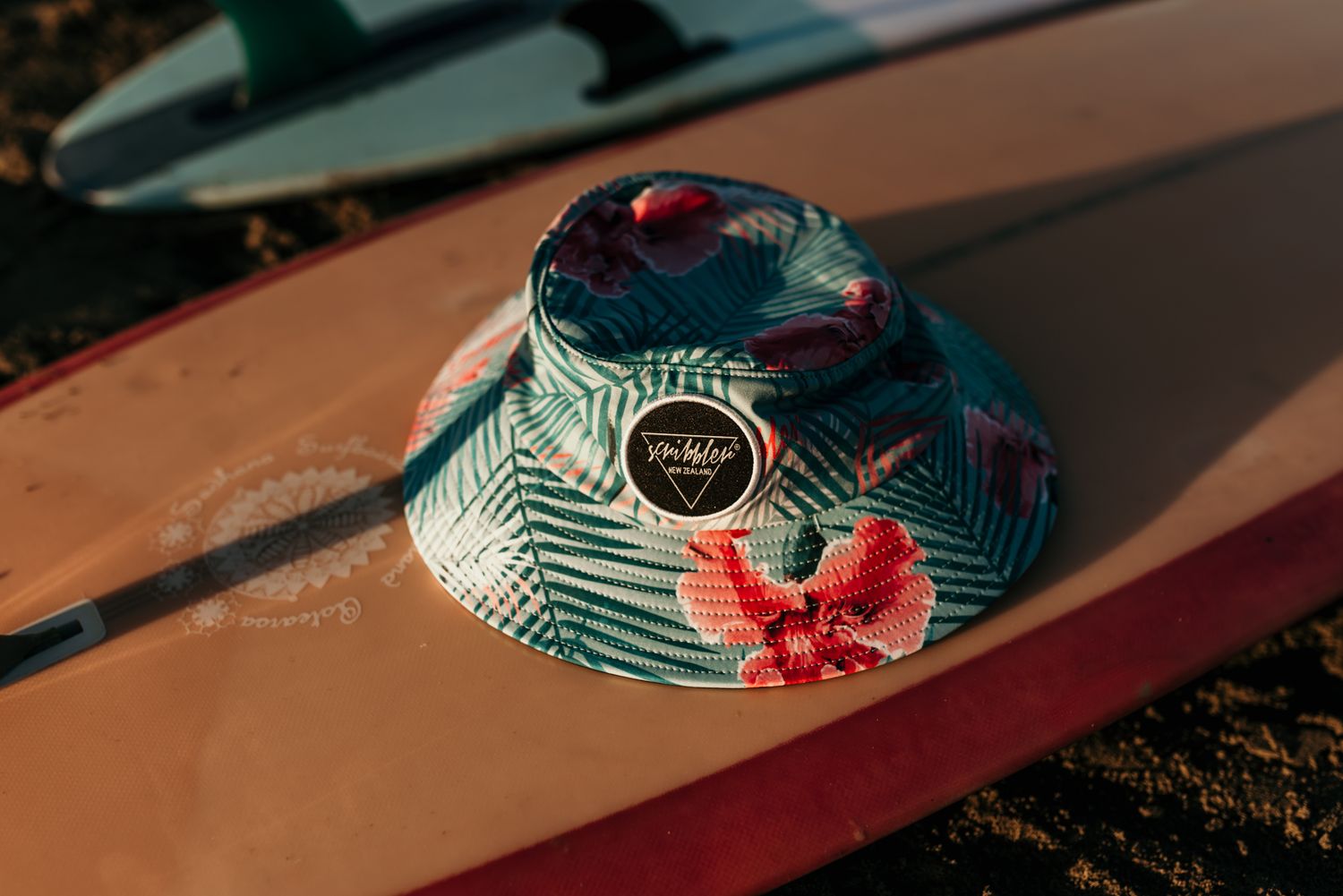 Colorful floral bucket hat with tropical pattern sitting on orange surfboard.