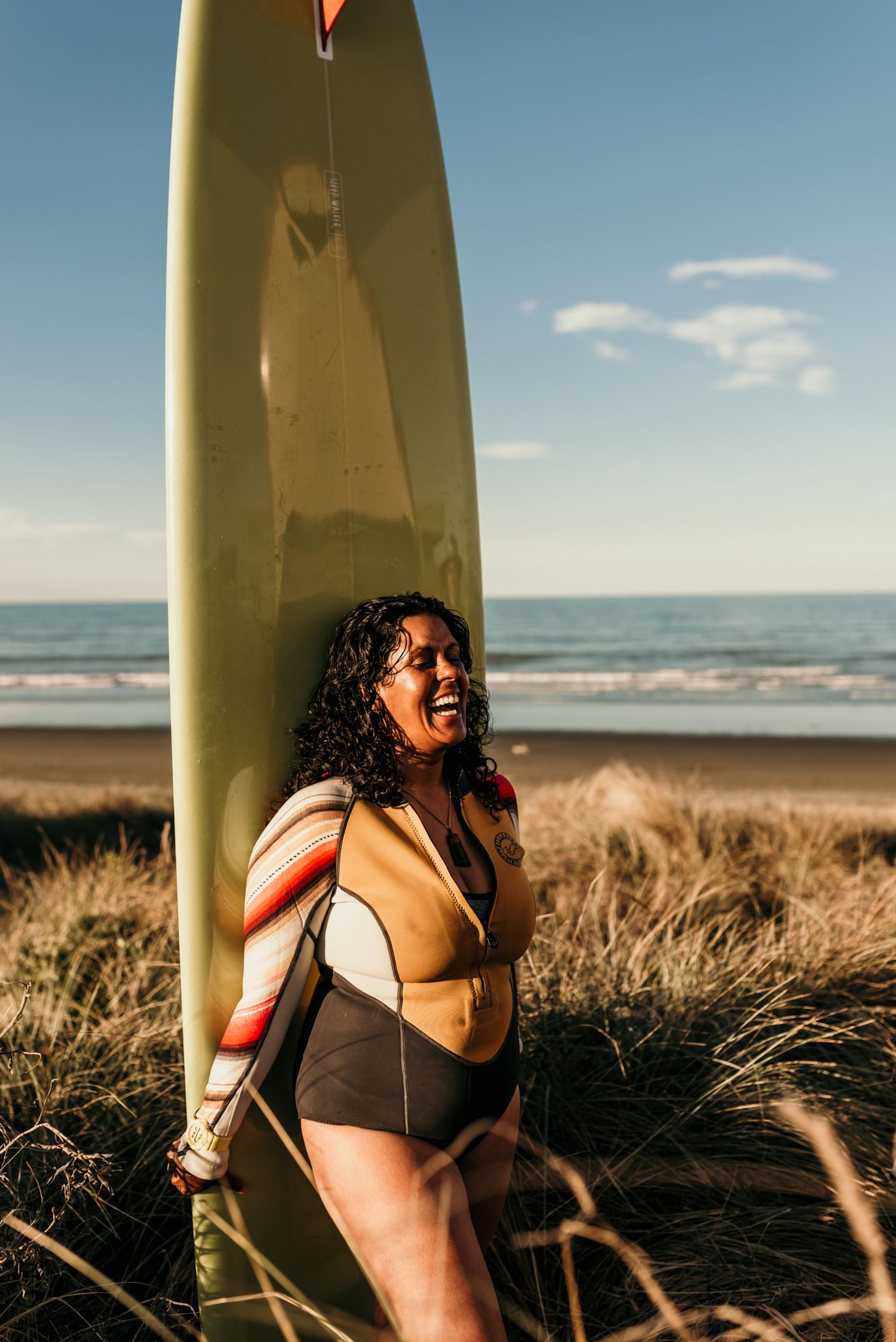 A surfer standing on the beach with a surfboard during golden hour.