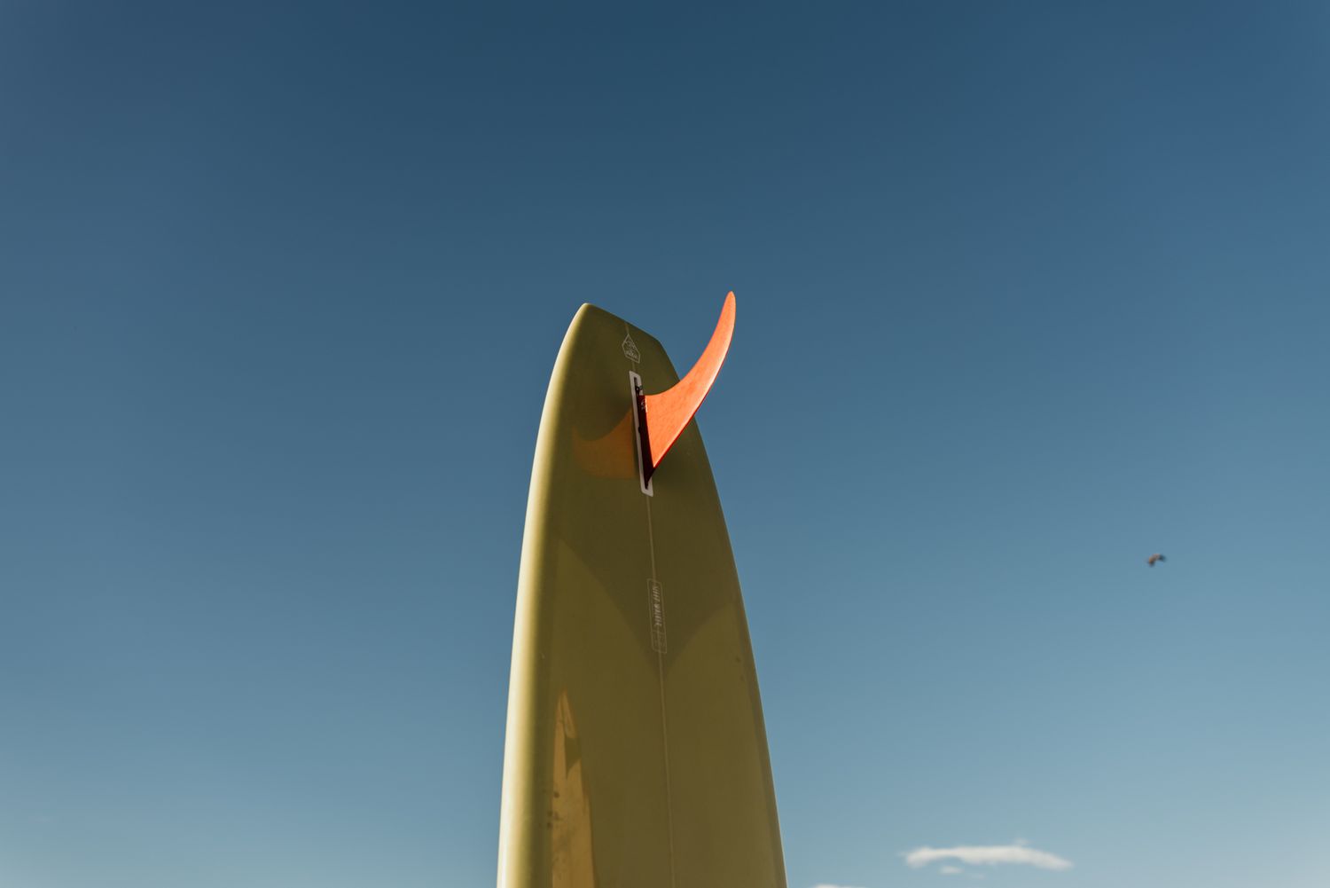 Close-up view of a surfboard fin against a bright blue sky.