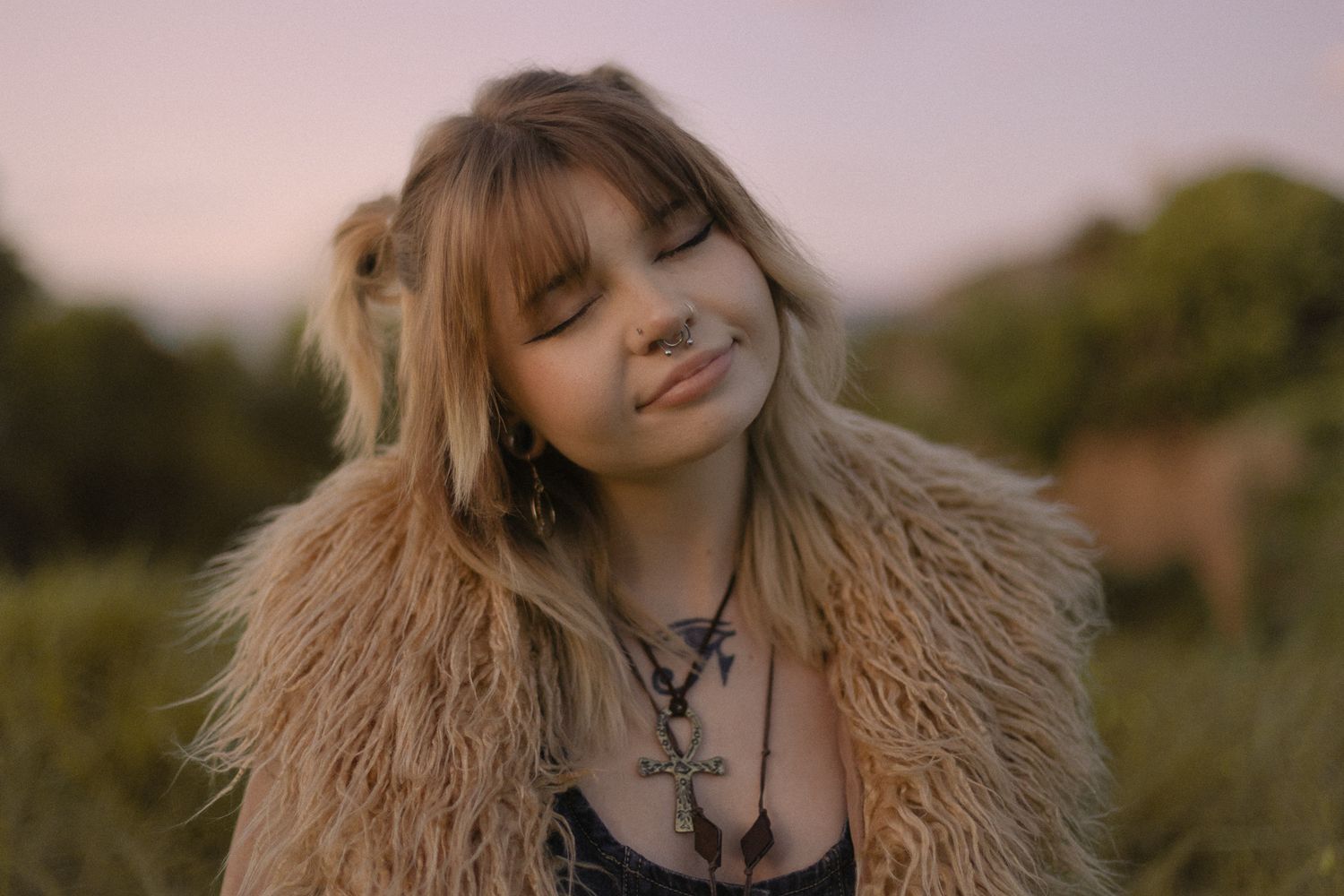 Person wearing fur coat posing against pink sunset sky.