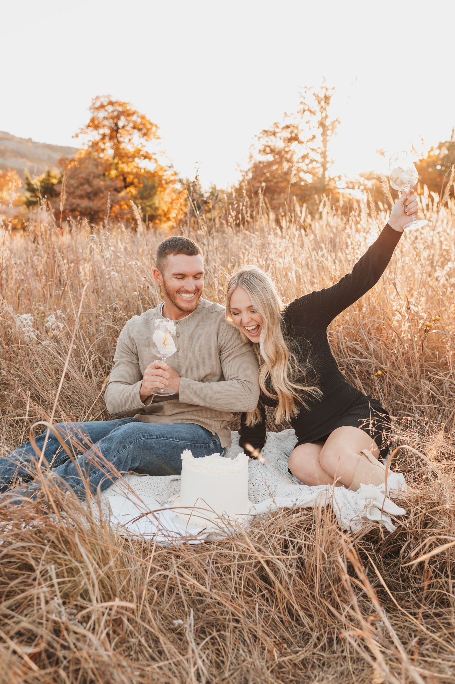 A smiling couple sitting on a picnic blanket in a golden field.