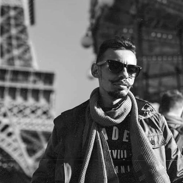 Black and white portrait of traveler with sunglasses and scarf near Eiffel Tower.