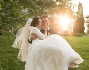 Romantic couple dancing in a grassy field at sunset with flowing white dress.
