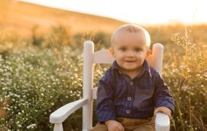 Child sitting in white chair among wildflowers at sunset.