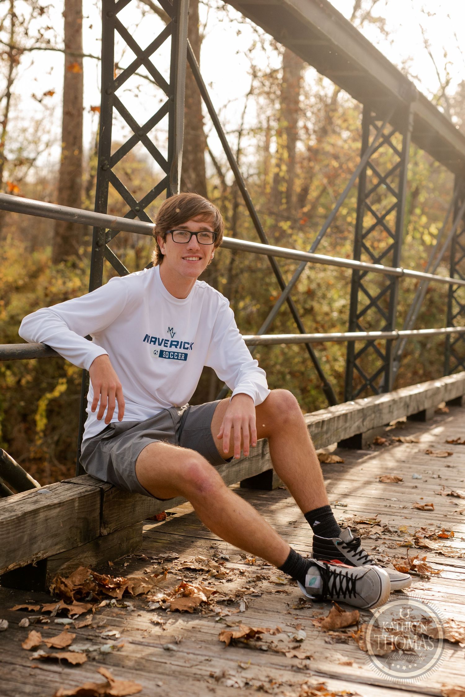 A person sits casually on a wooden bridge deck with metal railings during fall.