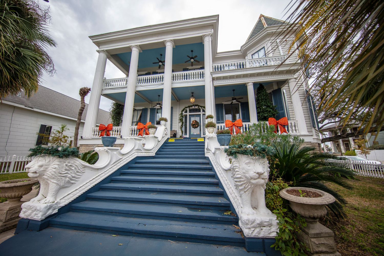 Grand southern-style mansion with blue stairs and white columns decorated with orange accents.