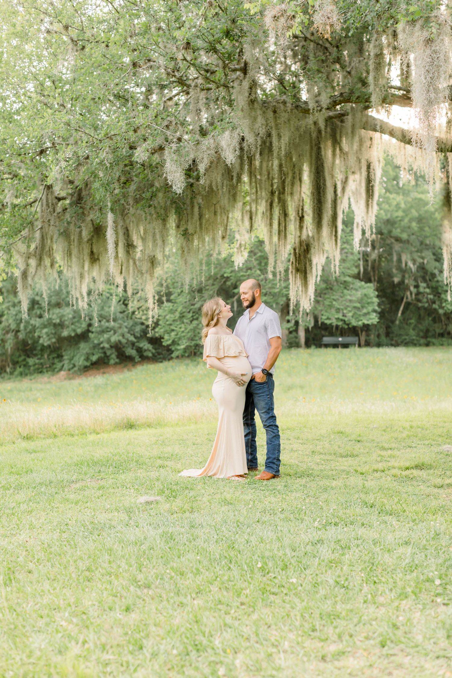 A couple stands together under dramatic Spanish moss in a Southern garden setting.