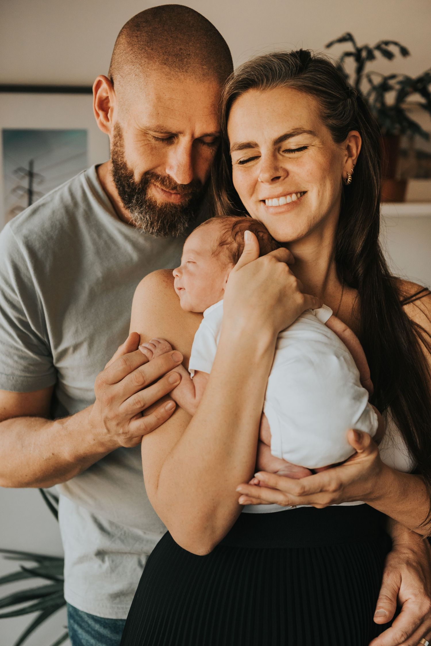 A loving couple shares a tender moment with their newborn baby in a warmly lit indoor setting.
