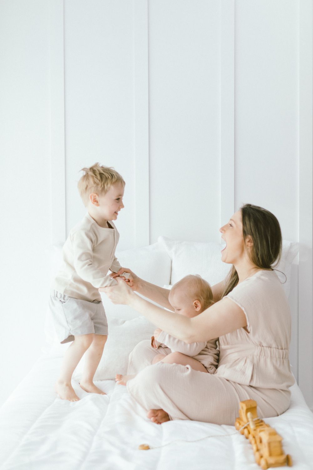 Energetic family playtime captured in light neutral tones against white backdrop.