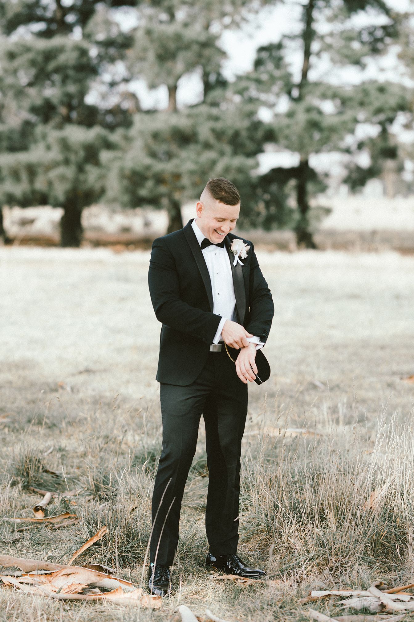 Groom in classic black tuxedo checking his watch in an outdoor setting.