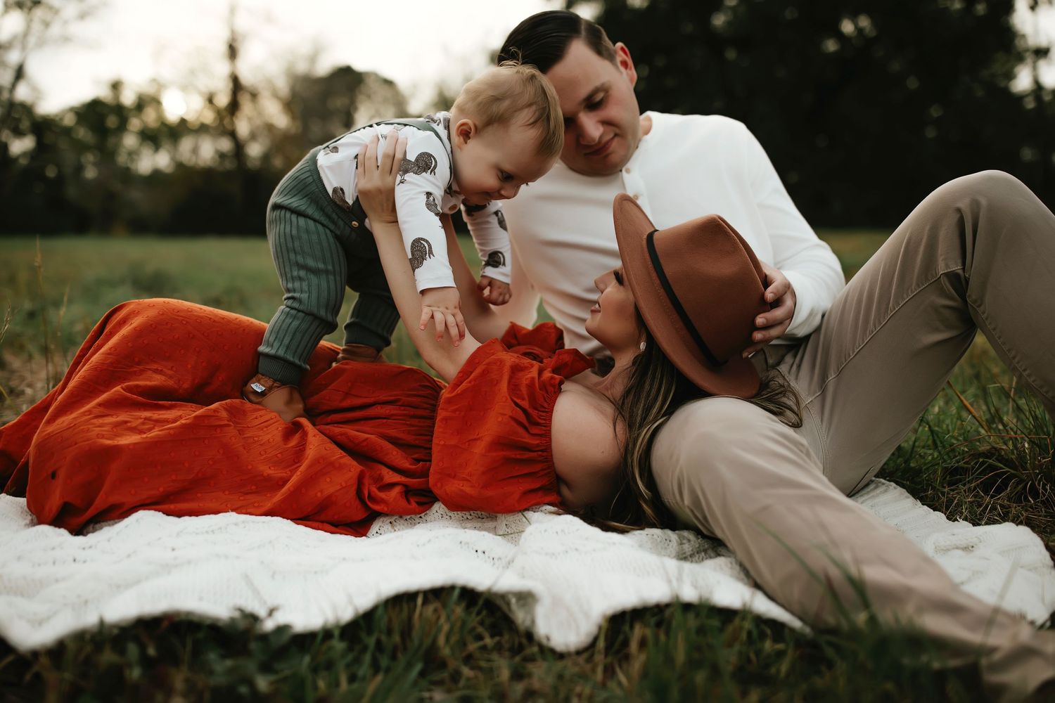 Family enjoying a picnic on a red blanket in a grassy field.