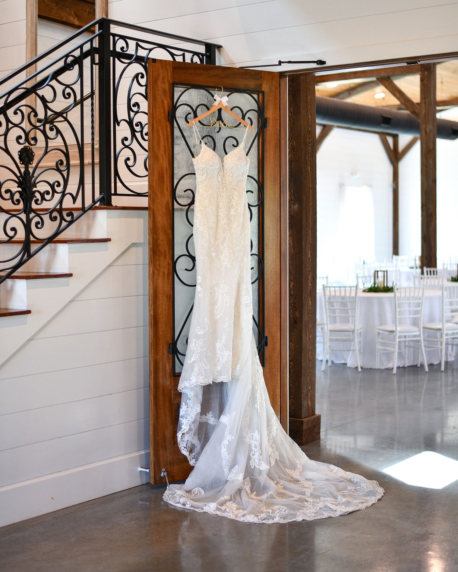 Wedding dress displayed on ornate iron staircase with long lace train flowing down.