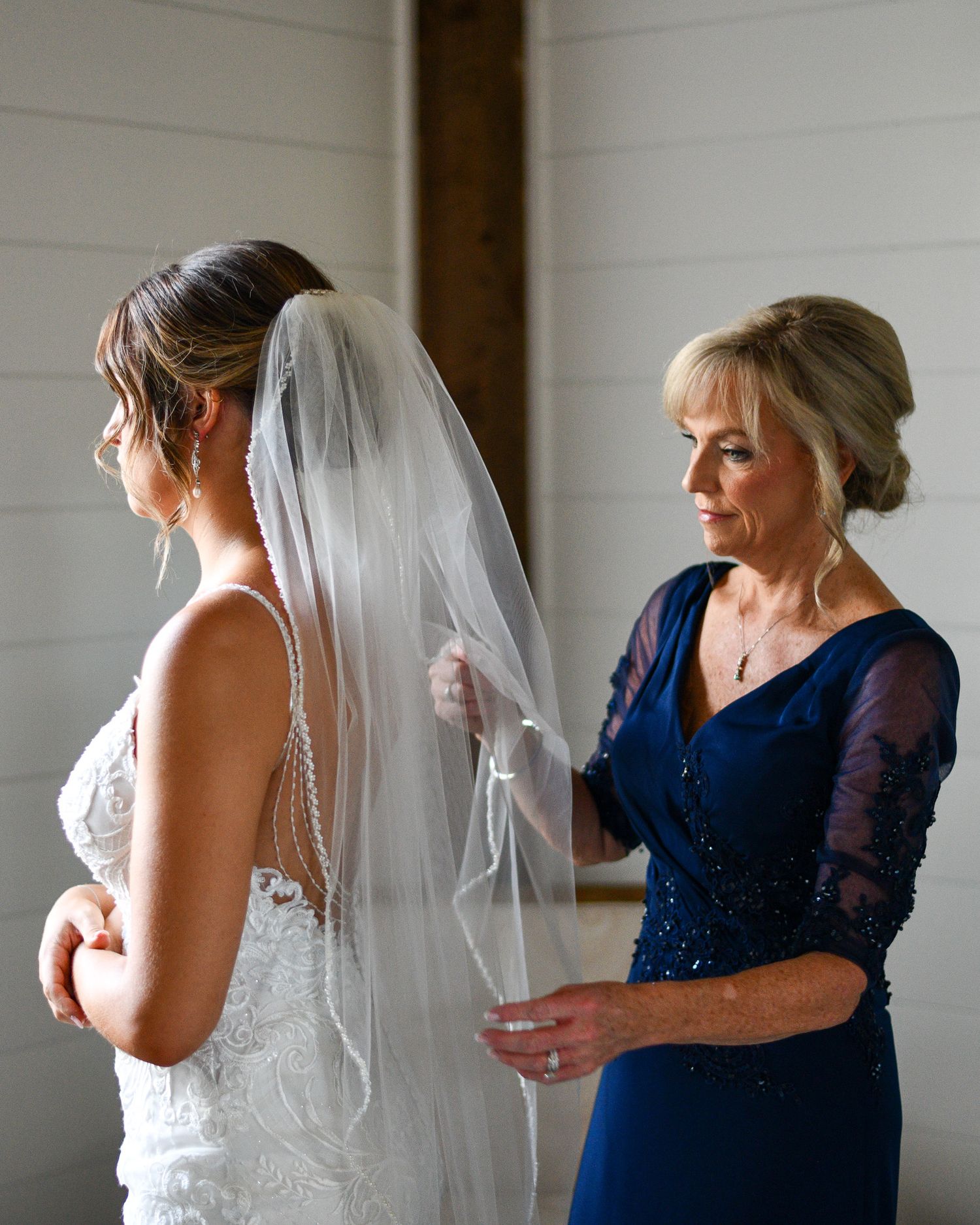 Final wedding preparation moment as veil is adjusted in natural window light.