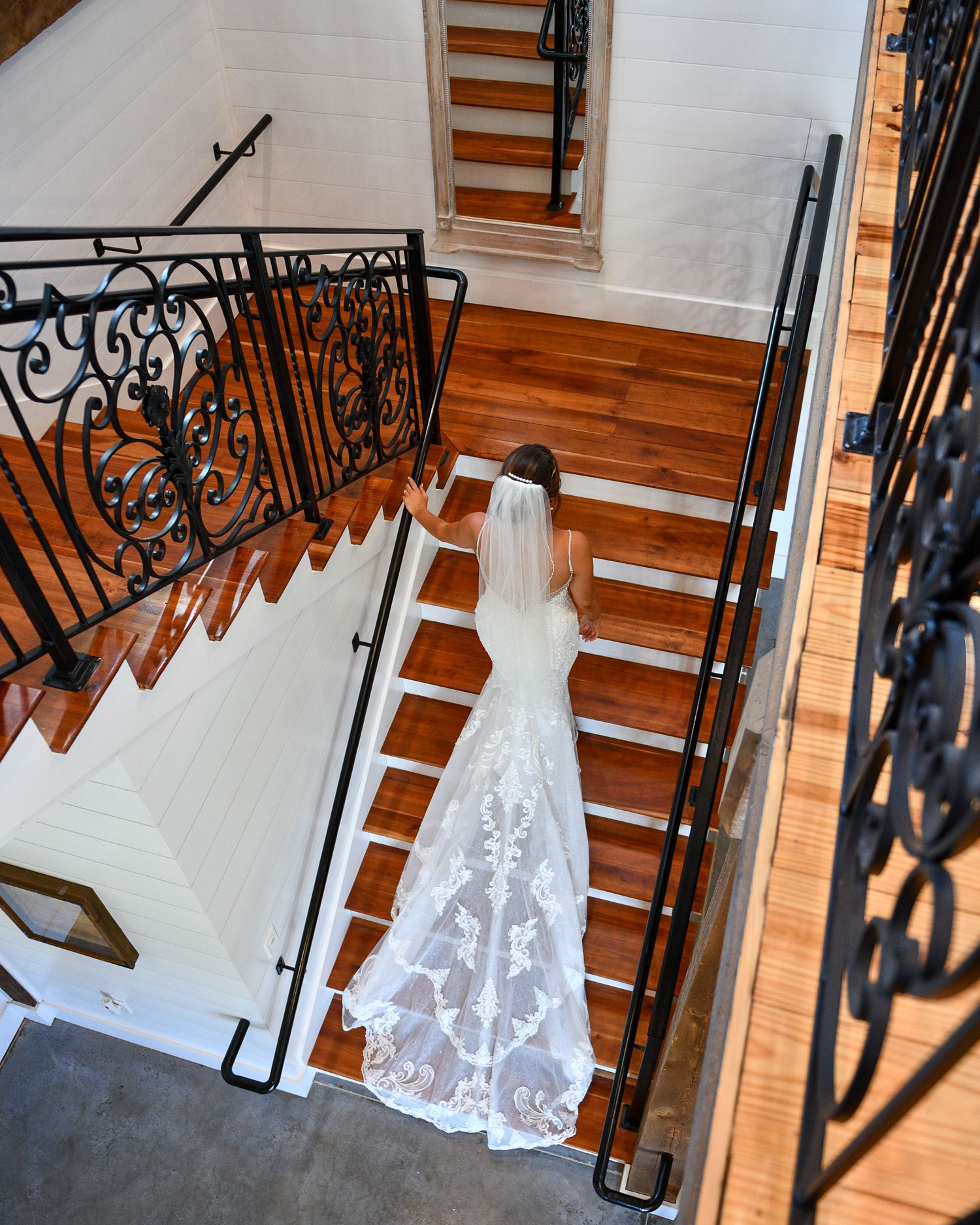 An elegant white lace wedding dress hanging on a staircase with ornate black iron railings and wooden steps.