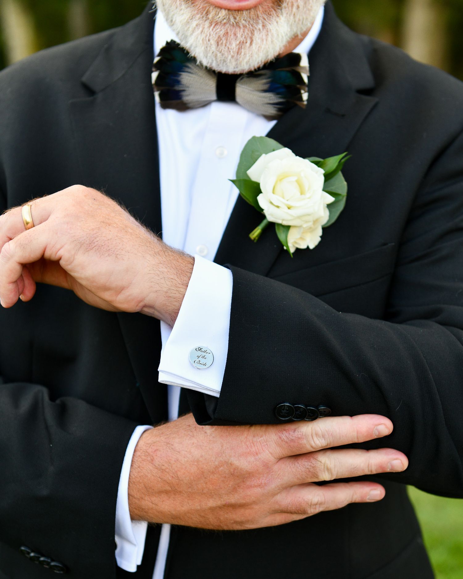 Close-up of formal wear details showing a black bowtie, white boutonniere, and cufflinks.